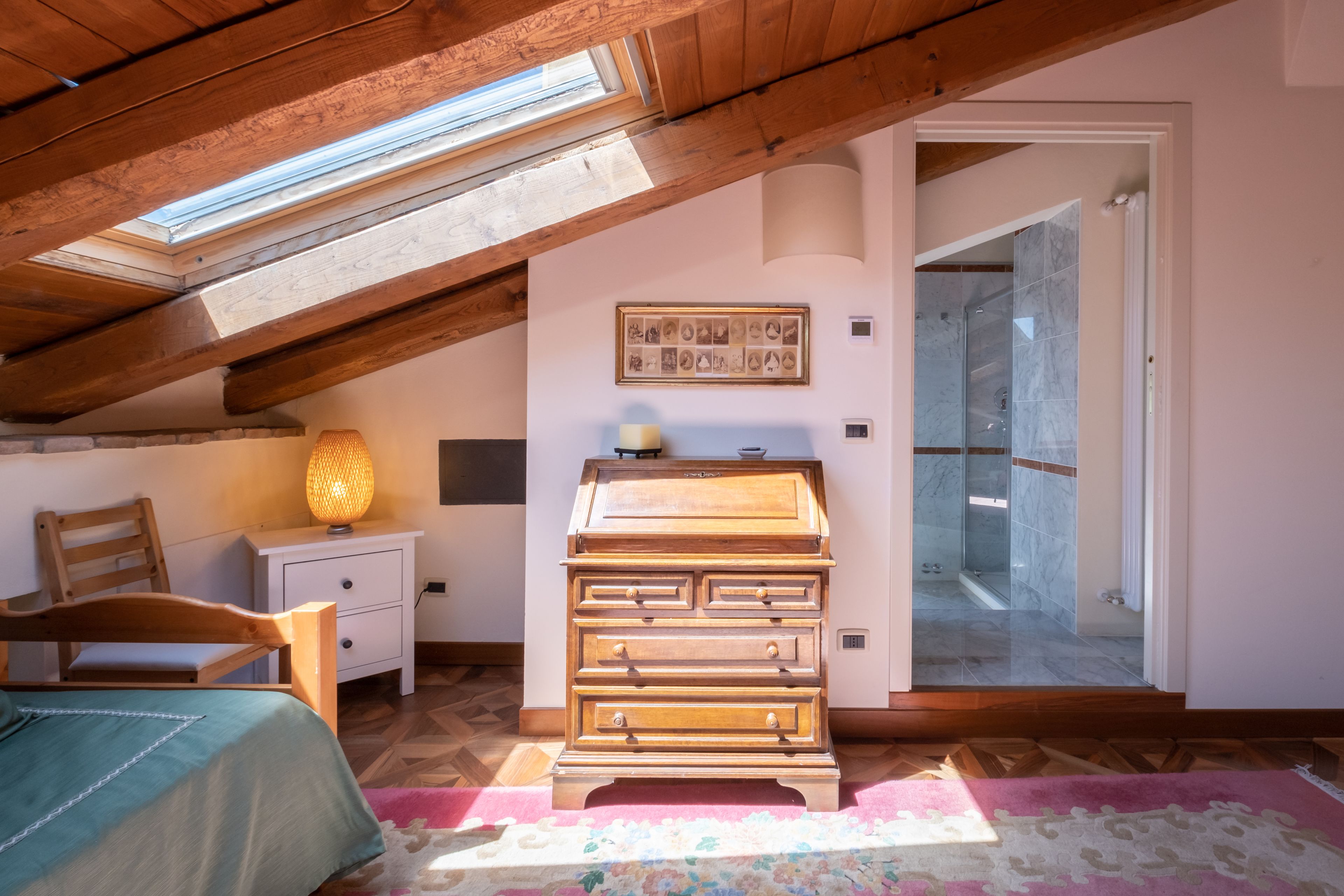 Een slaapkamer met een schuine kap, houten meubels, een bed, een dressoir en een dakraam.