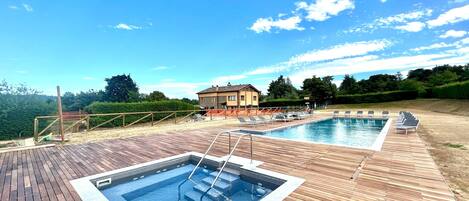 Eine Holzterrasse mit zwei rechteckigen Pools und Liegestühlen.