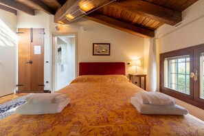 A bedroom with a wooden ceiling, a red headboard, a floral bedspread, and two towels on the bed. - Ca' Malvasia - BolognaRooms (Sasso Marconi)