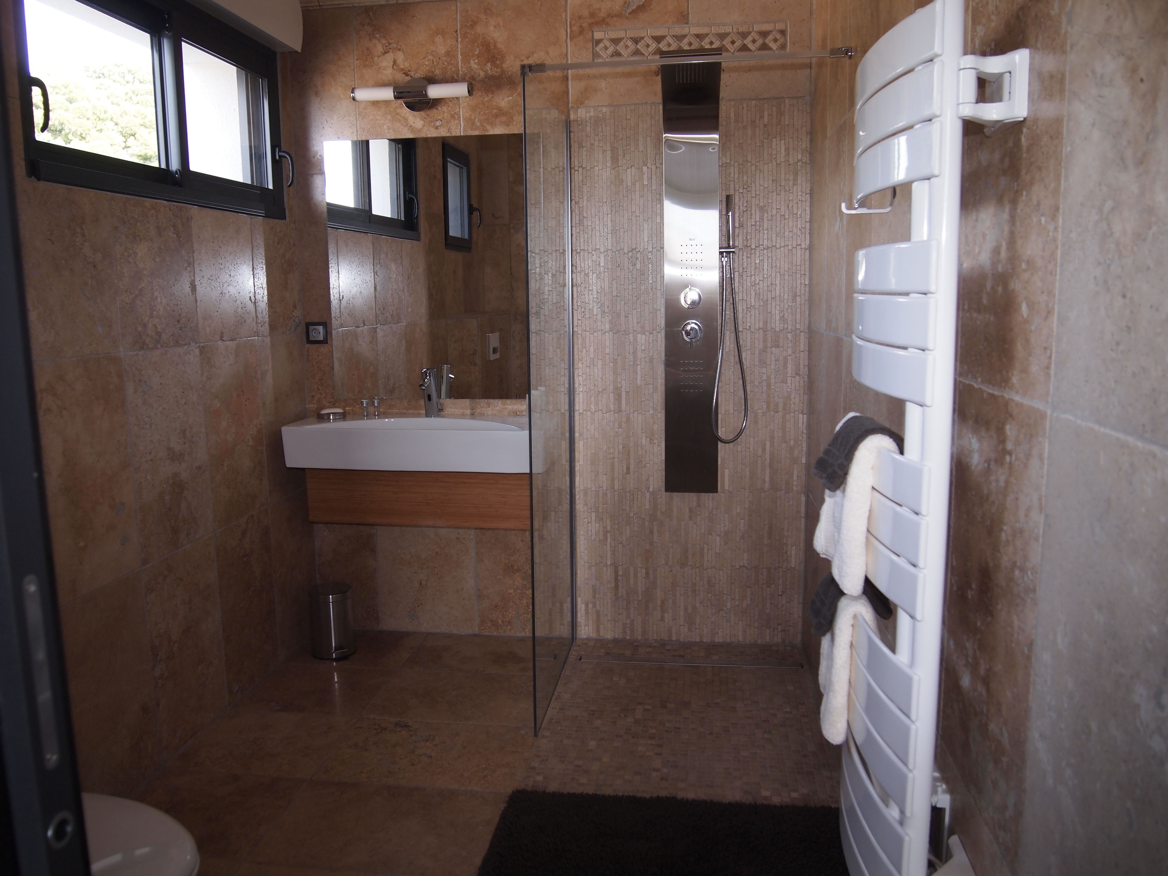 A modern bathroom with a glass-enclosed shower, a large sink, and a towel rack.