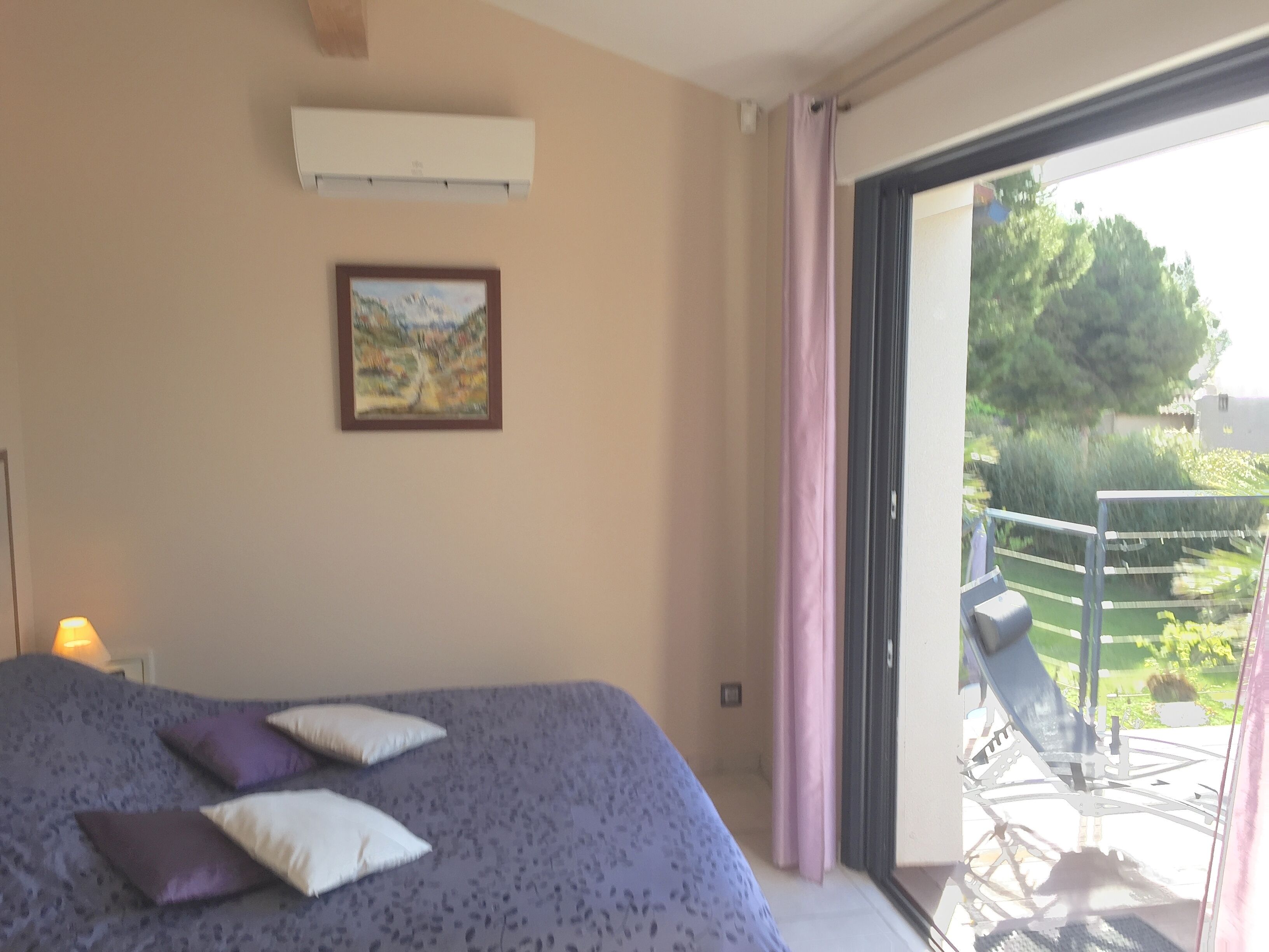 A bedroom with a bed, a painting, and a view of a balcony with outdoor furniture.