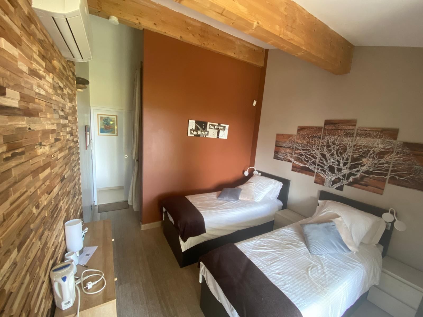 Een hotelkamer met twee bedden, een houten wand, een bruine deur en een plafond met zichtbare balken.