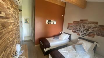 Een hotelkamer met twee bedden, een houten wand, een bruine deur en een plafond met zichtbare balken.