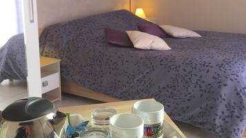A bedroom with a bed, a bedside table, a lamp, and a tray with a kettle, cups, and jars.