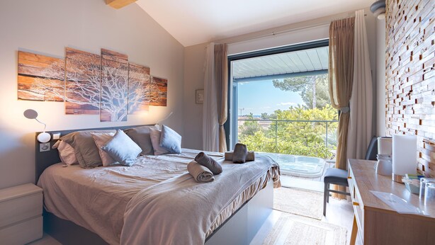 A modern bedroom with a large bed, a desk, and a view of greenery outside. - B&B L'Escale Cote Bleue (Sausset-les-Pins)