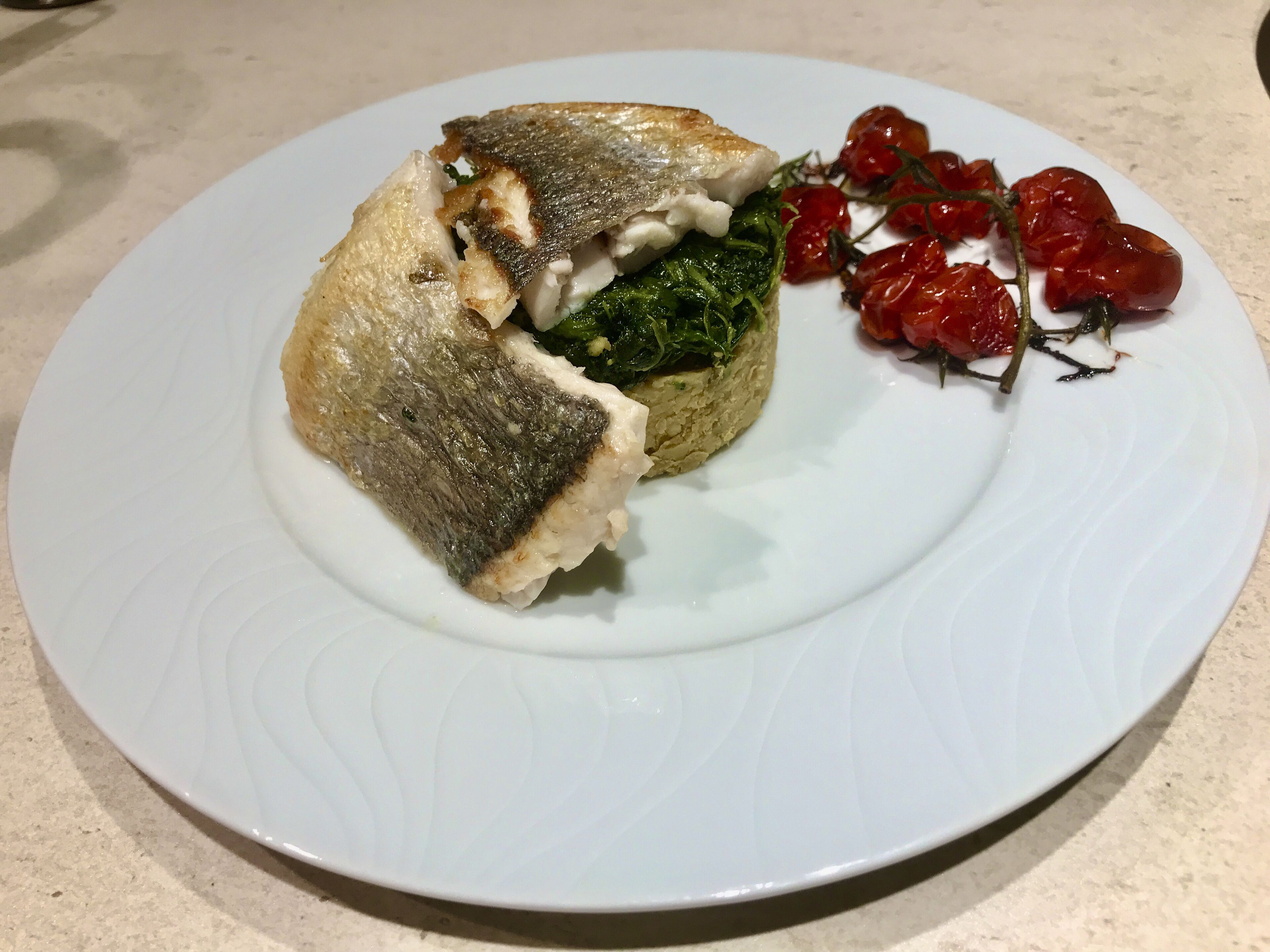 A plate with a piece of fish, a mound of greens, and cherry tomatoes.