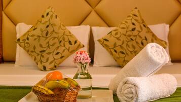 Quarto bem arrumado com cama, almofadas, cesta de frutas, vaso com flores e toalhas dobradas.