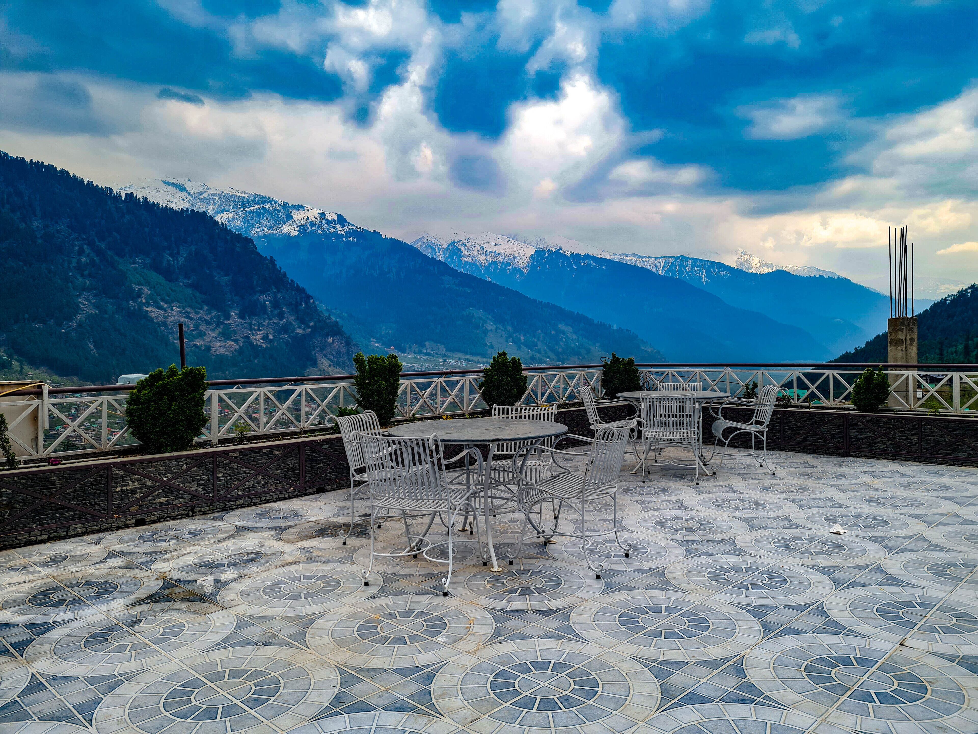 A terrace with tables and chairs, overlooking snow-capped mountains.