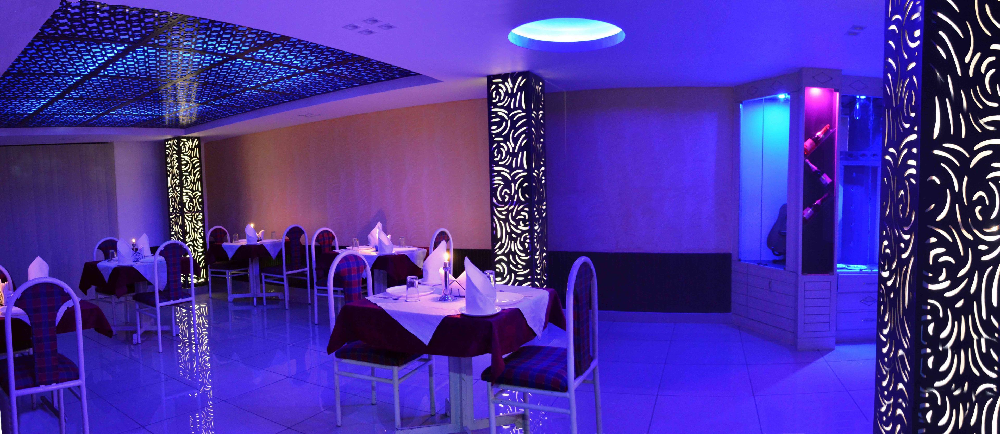 A dining area with tables set for service, a patterned wall, and a ceiling with a geometric light fixture.