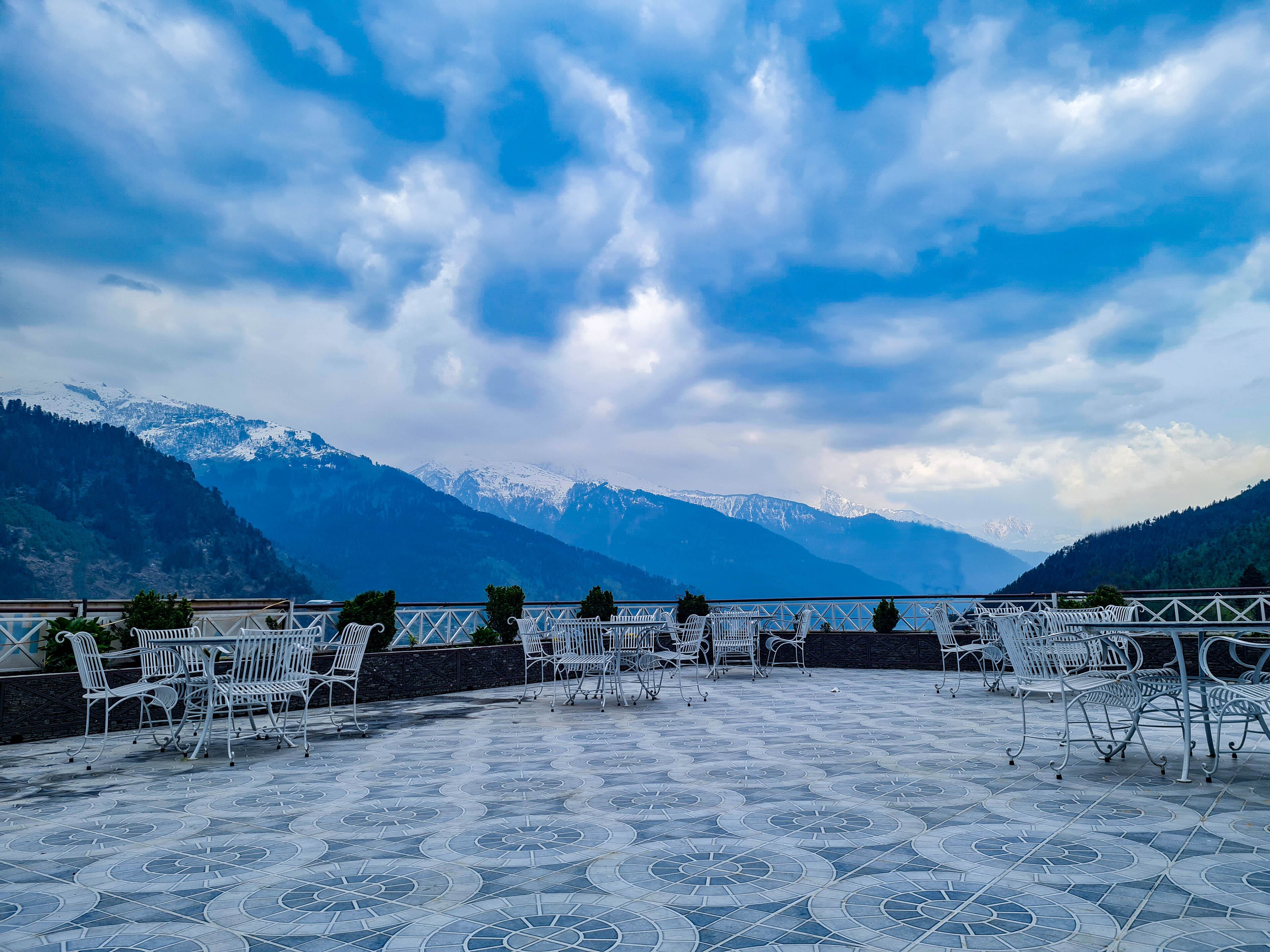 Una terrazza con pavimento decorato e sedie in metallo bianco, con vista su un lago e montagne innevate.