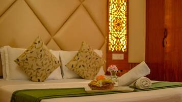 A neatly made bed with two patterned pillows, a green throw blanket, a small basket with fruits, and a rolled towel.