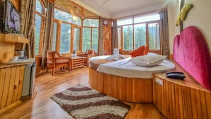 A cozy room with a bed, a desk, and a chair. There are large windows with curtains, a ceiling fan, and a clock on the wall. - Hotel Mountain Top (Manali)