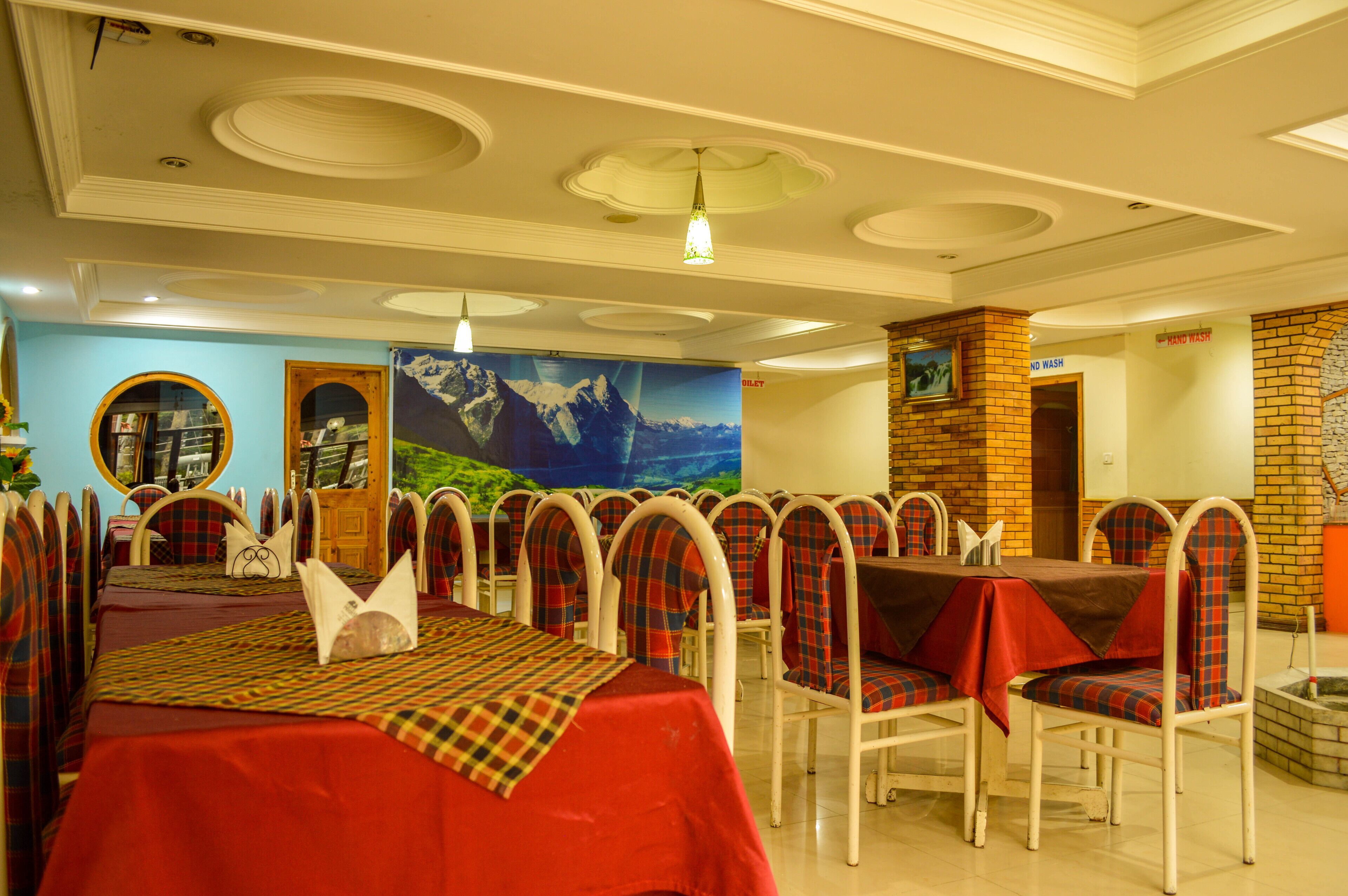 Un restaurante con mesas y sillas redondas, un mural en la pared y un dispensador de jabón.