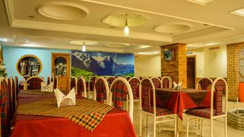 Un restaurante con mesas y sillas redondas, un mural en la pared y un dispensador de jabón.