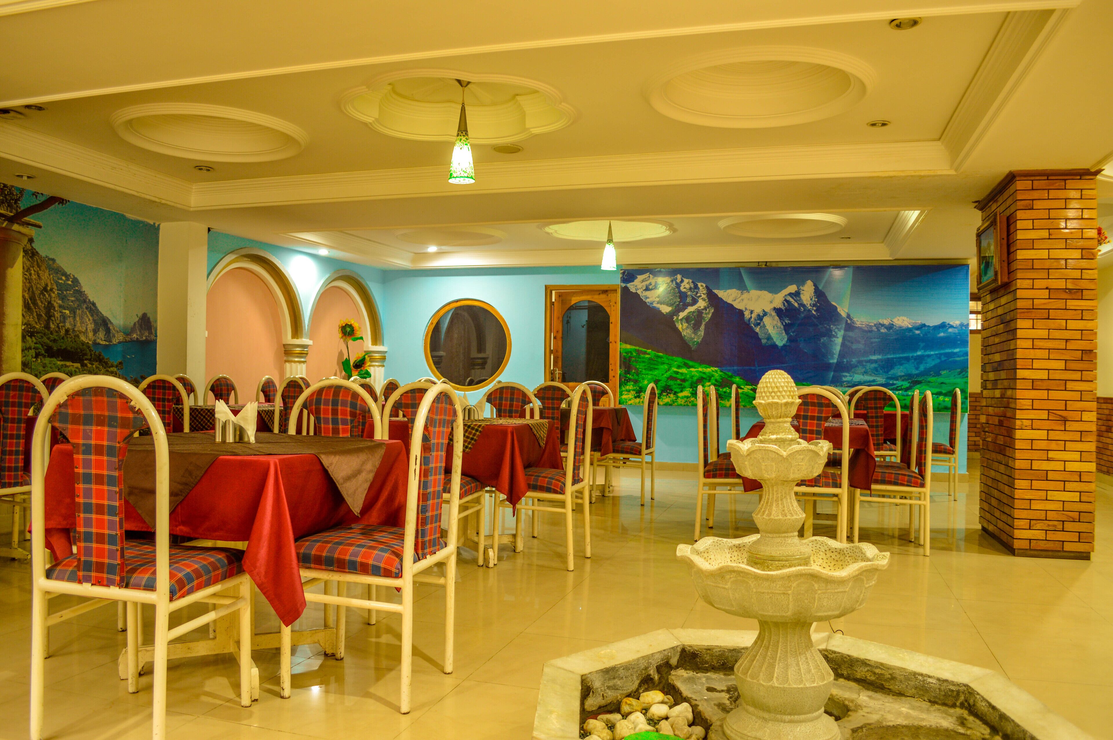 Un espace repas avec des tables et des chaises rondes, une fontaine et des peintures murales.