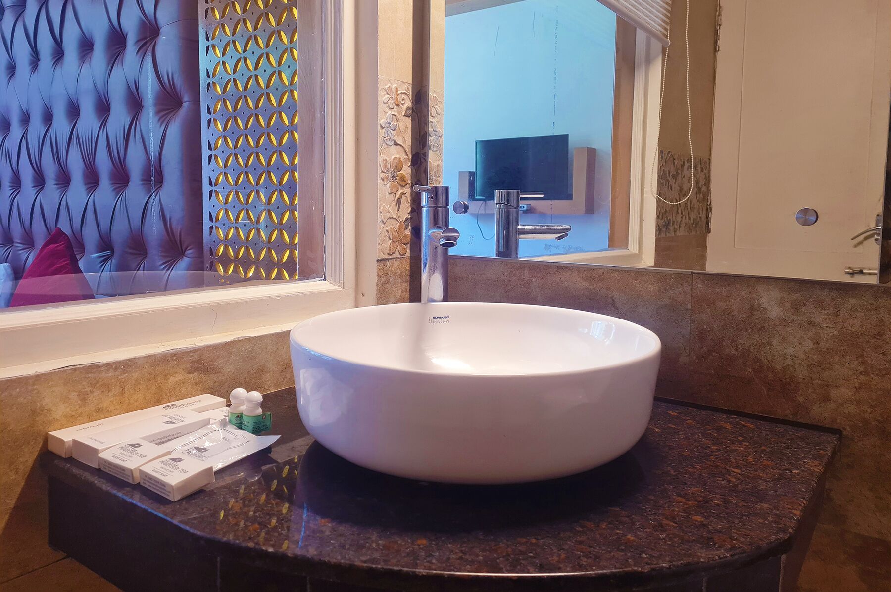 Une salle de bain avec un lavabo rond blanc, un miroir et une fenêtre ornée d’un motif décoratif.