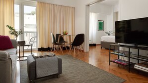 A modern living room with a sofa, a coffee table, a TV, and a dining area with chairs and a table. - Parthenon Apartment (Athens)