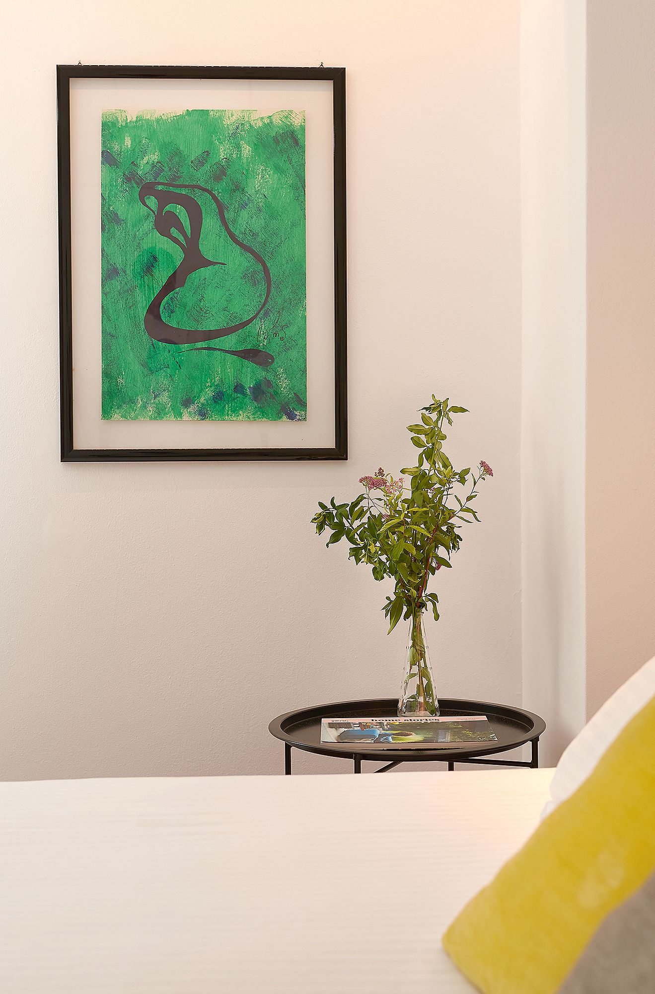 A framed abstract painting, a small table with a vase of flowers, and a magazine on the table.