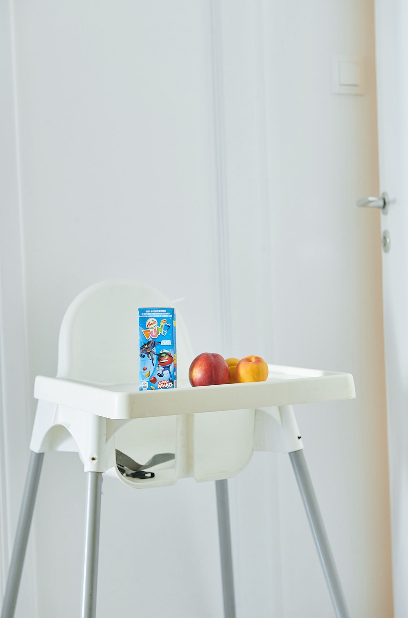 A white high chair with a blue cereal box and two apples on the tray.