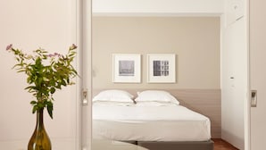 A hotel room with a bed, a bedside table with a vase, and two framed pictures on the wall. - Parthenon Apartment (Athens)