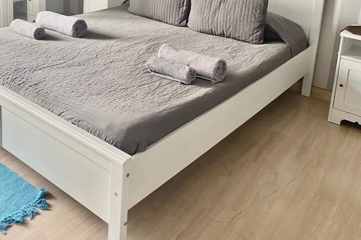 Un lit bien fait, avec une tête de lit à rayures, une table de chevet avec une lampe et un tapis bleu sur un plancher en bois.