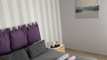 Un dormitorio moderno con cama, almohadas, una mesita de noche, lámpara y un cuadro en la pared.