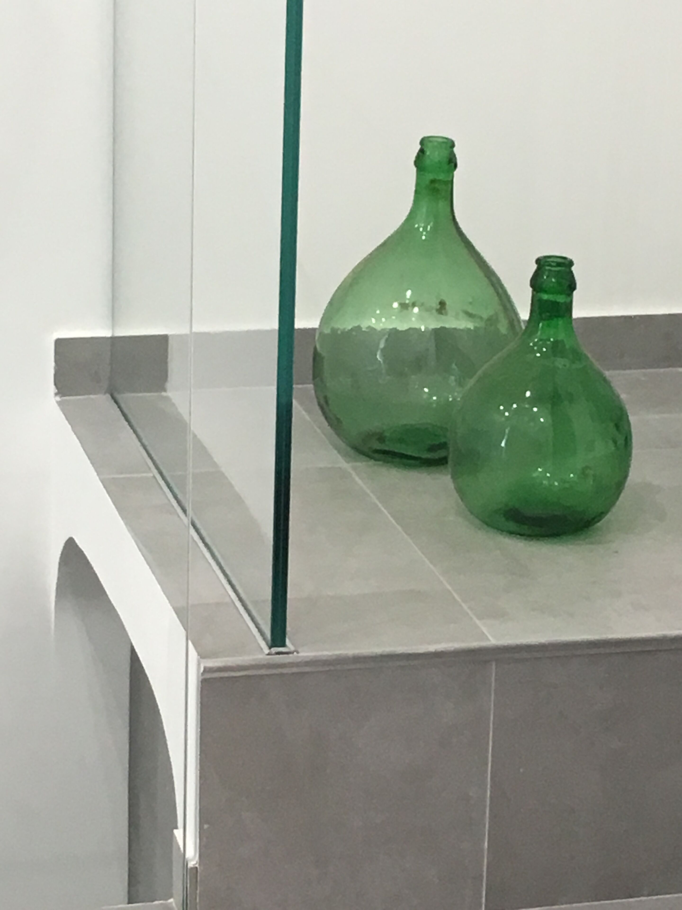 Two green glass bottles on a tiled surface with a vertical green pole.