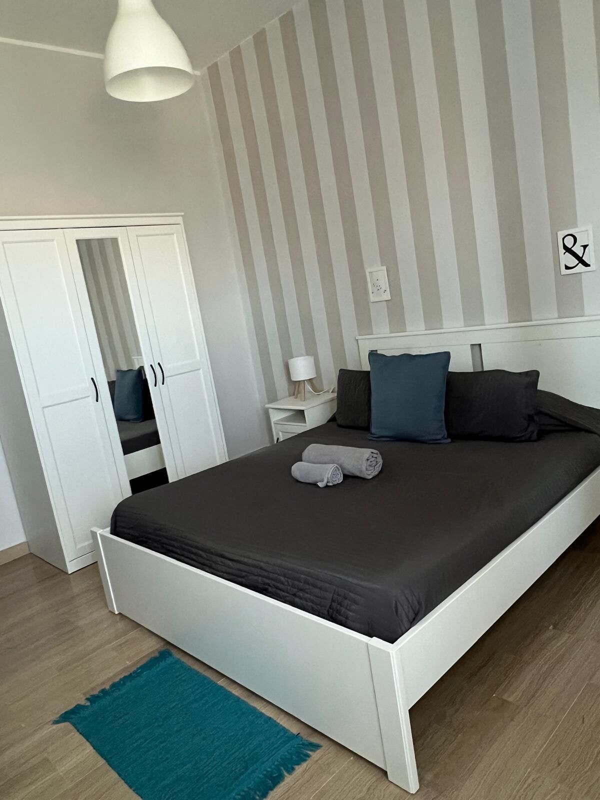 Un dormitorio con cama, mesita de noche, lámpara, armario y pared a rayas.