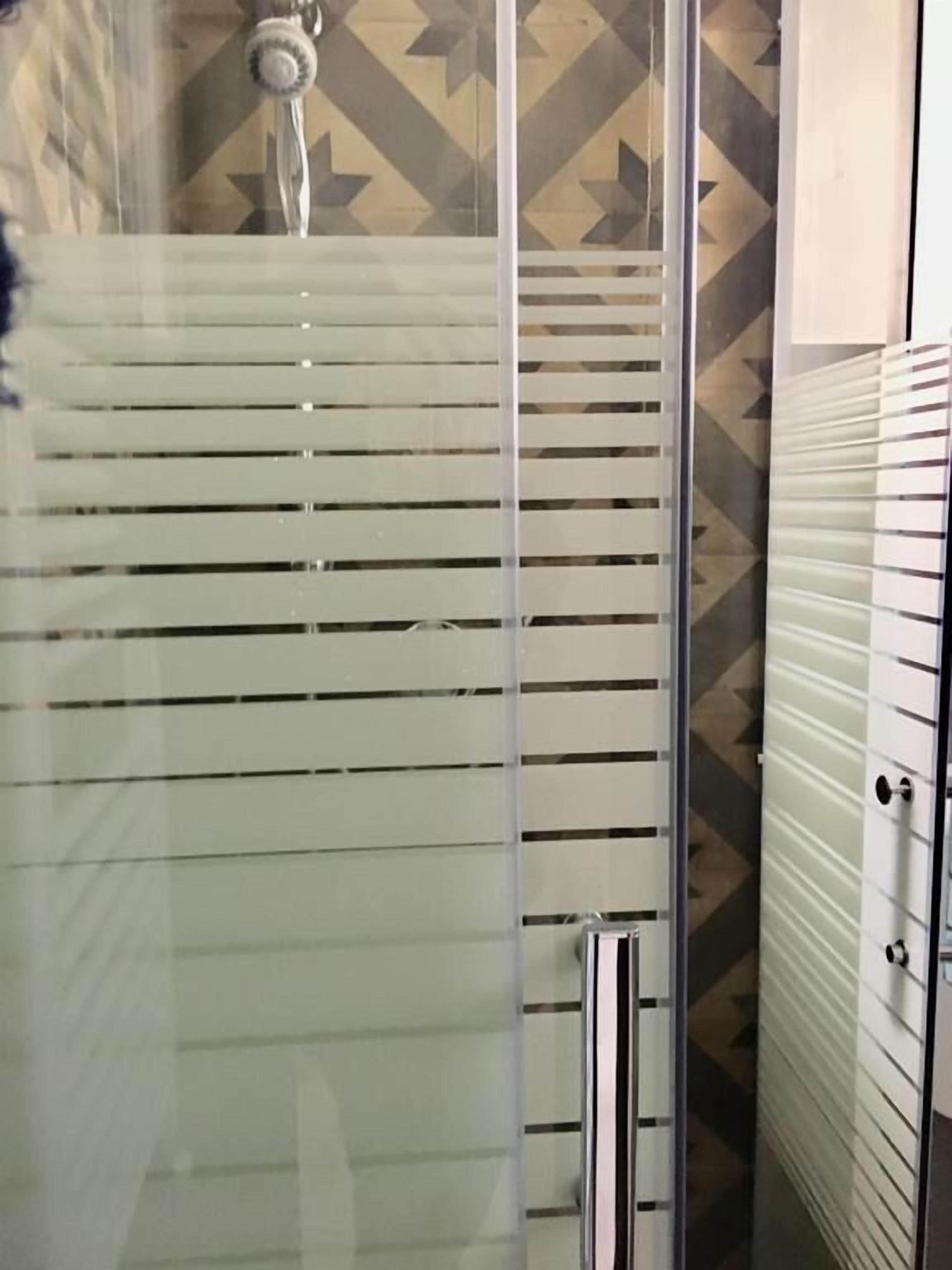 A glass-enclosed shower with horizontal blinds, a patterned wall, and a metallic door.