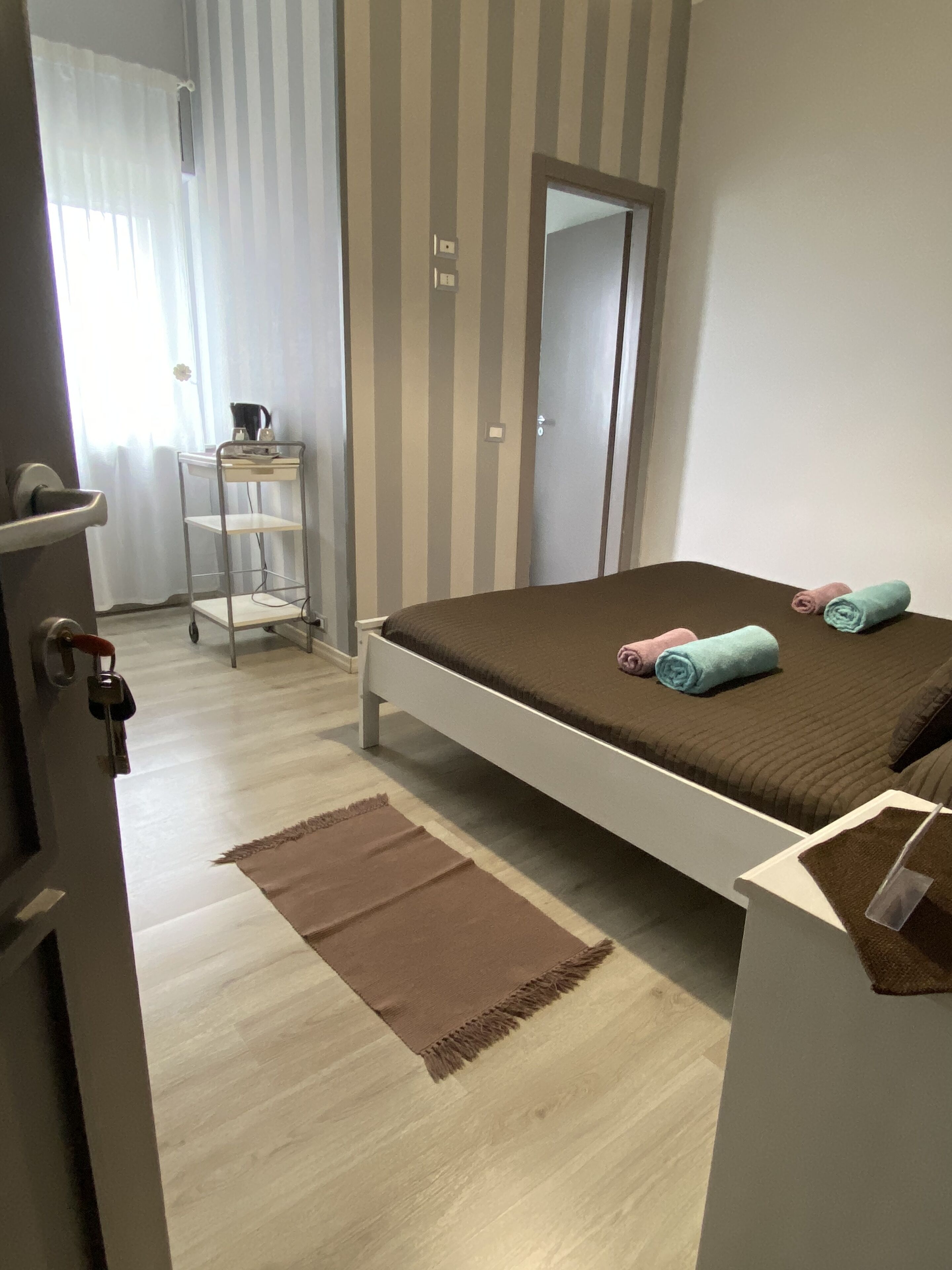 Une chambre à coucher comprenant un lit, une table de chevet, un miroir, une armoire, une petite étagère et une porte avec des clés.