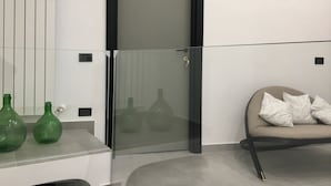 A modern room with a glass door marked 'D', a sofa with cushions, and green vases on a white console.