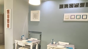 A dining area with two white tables and chairs, a light fixture, and framed pictures on the wall.