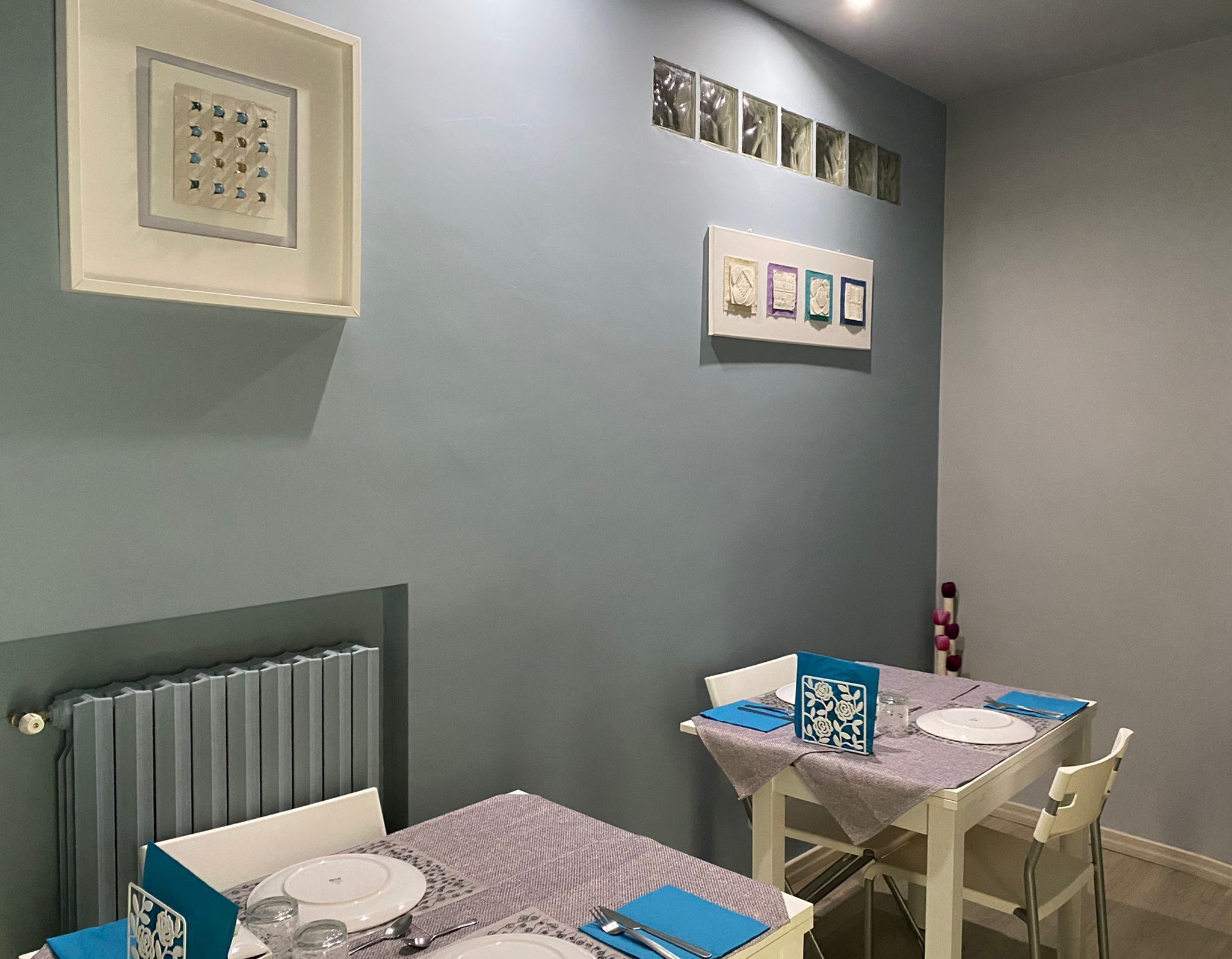 Un comedor con dos mesas dispuestas para dos comensales, cada una con platos, cubiertos y servilletas.