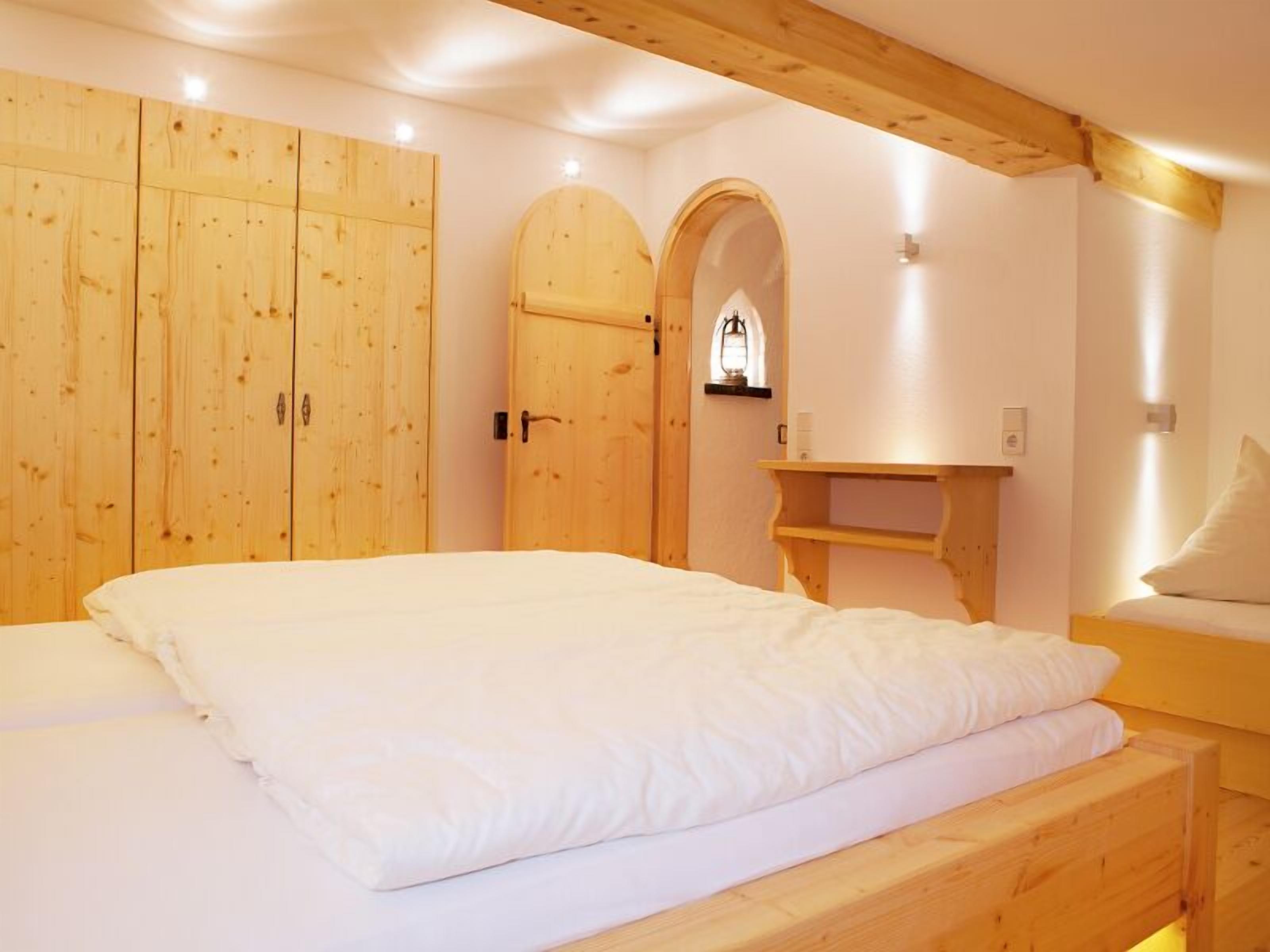 Une chambre avec un lit en bois, une armoire et une petite fenêtre ornée d’une lanterne.