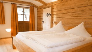 Ein Bett mit Holzrahmen und weißer Bettwäsche in einem Zimmer mit Holzwänden und einer Holztür.