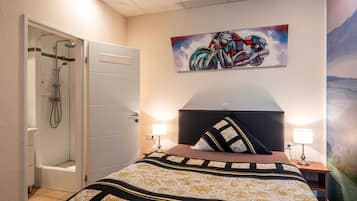 Quarto de hotel com cama, chuveiro, quadro e mesa de cabeceira.