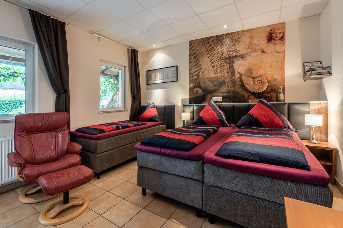 Een hotelkamer met een groot bed, twee banken, een rode leren fauteuil en een groot schilderij aan de muur.
