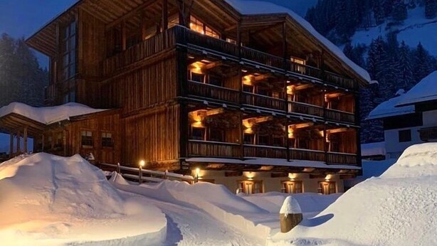 Un refugio de madera de varios pisos con balcones, rodeado de terreno nevado y un paisaje montañoso.