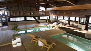 Una amplia piscina interior con solárium de madera y zona de estar con cubierta de madera.