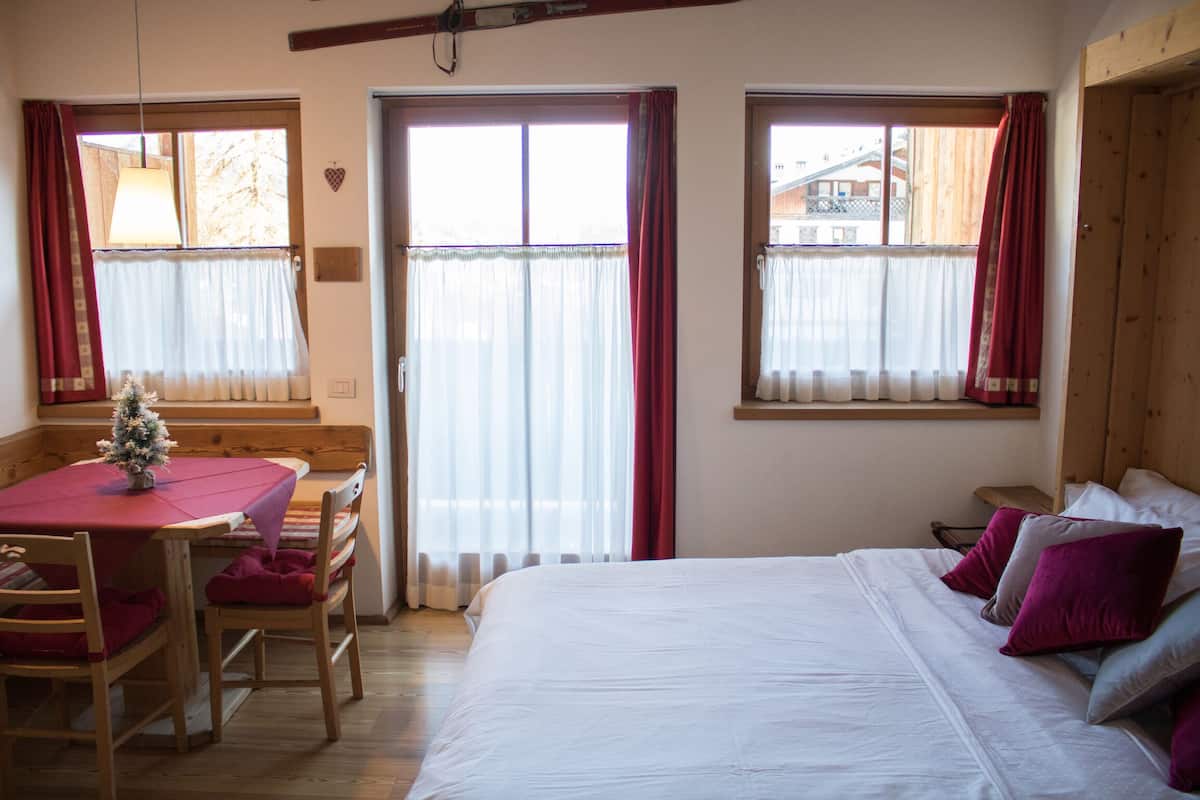 A bedroom with a bed, a small table with chairs, and a window with curtains.