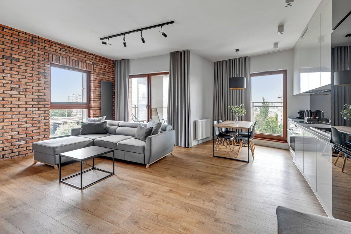 A modern living room with a sectional sofa, a dining area with a table and chairs, and a kitchen with a stove and cabinets.