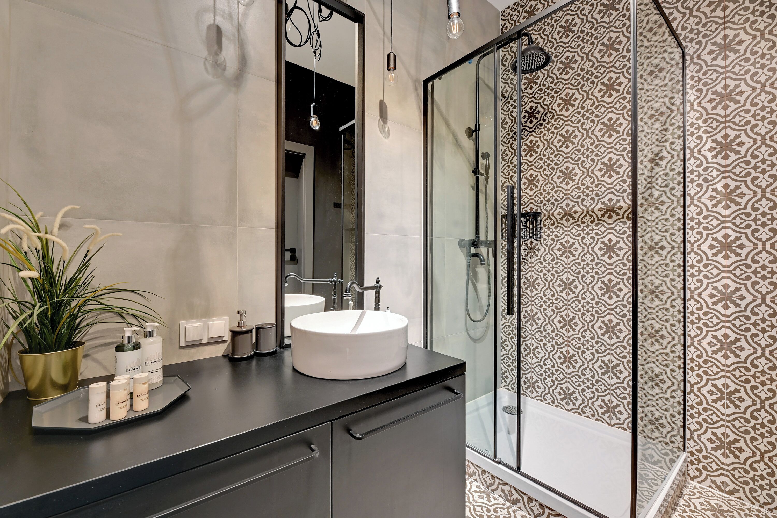 Ein modernes Badezimmer mit einem runden Waschbecken, einer Duschkabine aus Glas und Wandfliesen mit Muster.