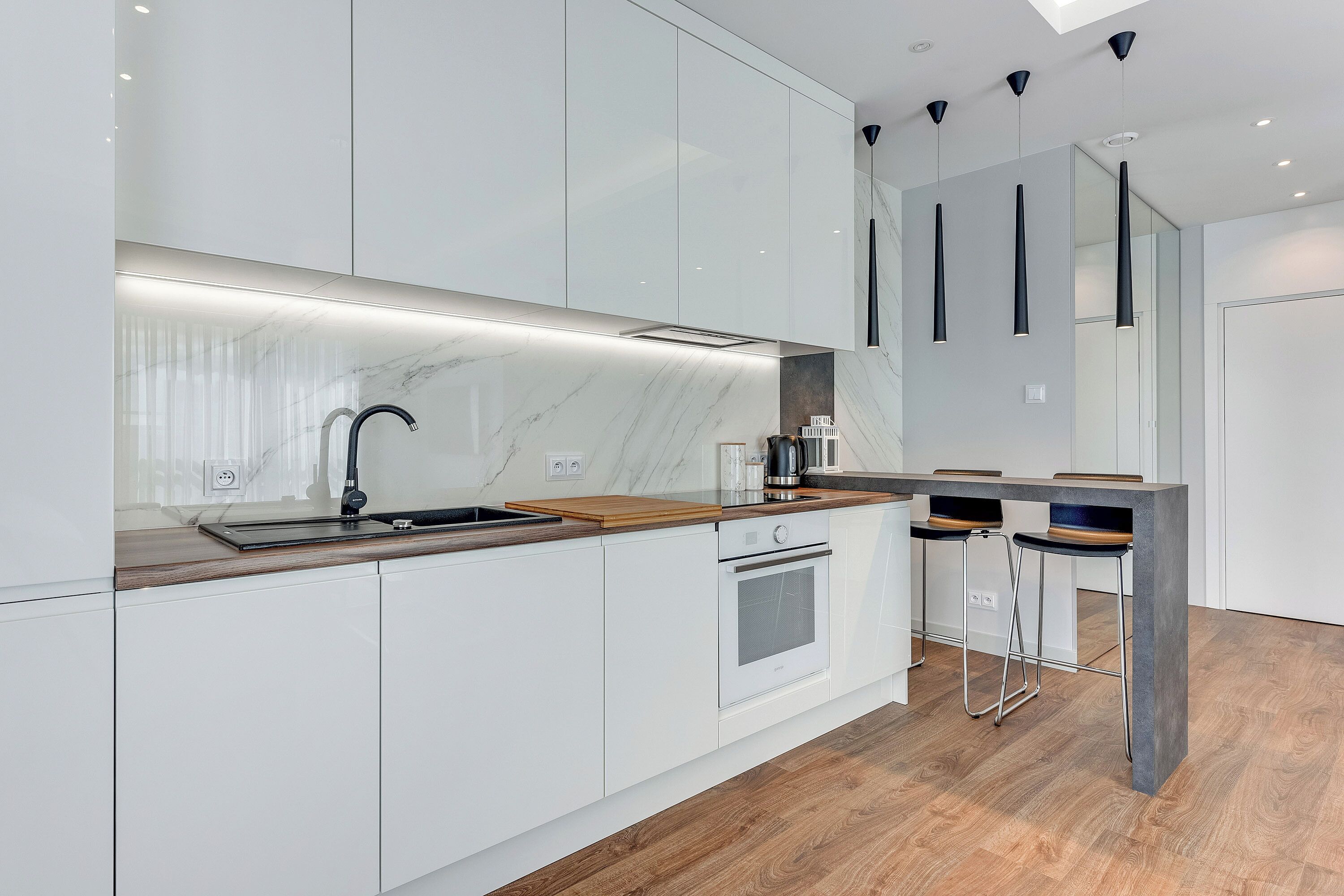 A modern kitchen with white cabinetry, a wooden countertop, a built-in oven, and a bar area with stools.