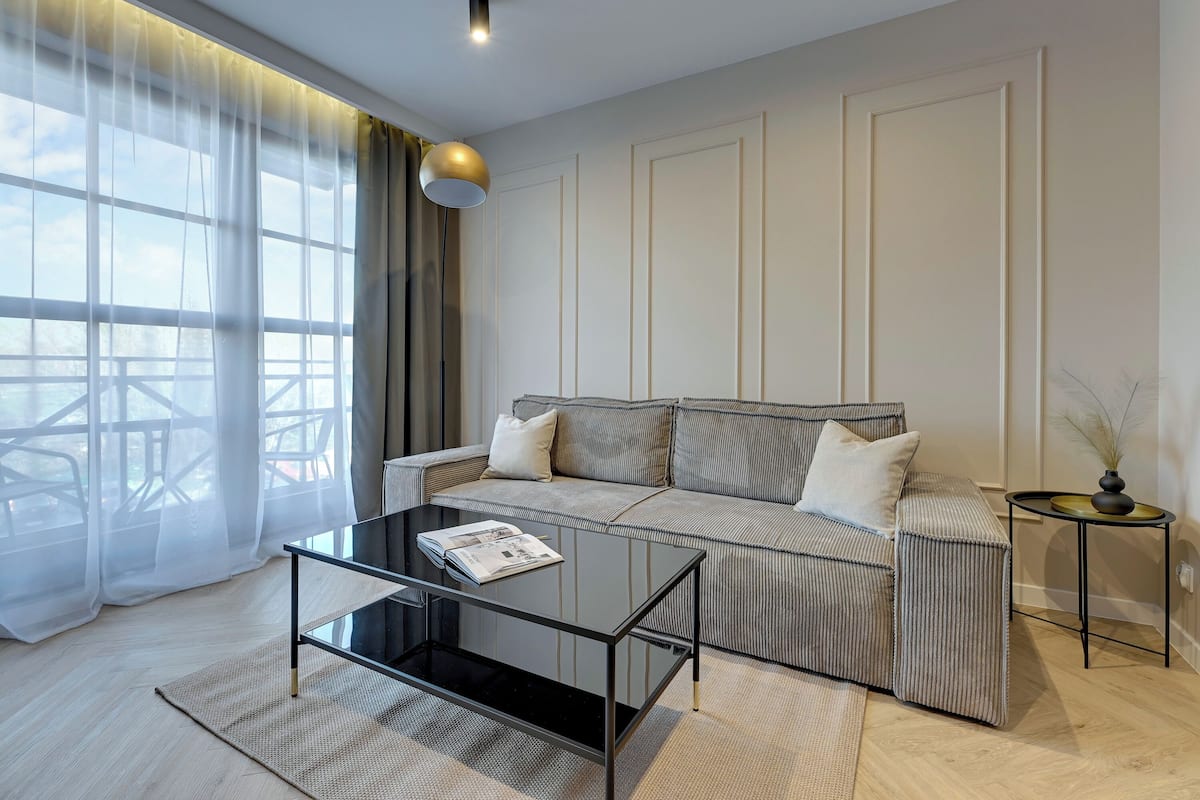 A modern living room with a sofa, a glass coffee table, and a side table with a lamp.