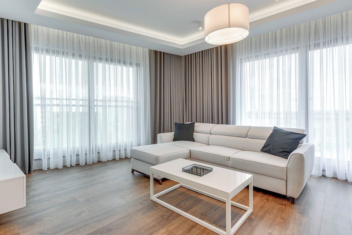 A modern living room with a sectional sofa, a coffee table, and large windows with sheer curtains.
