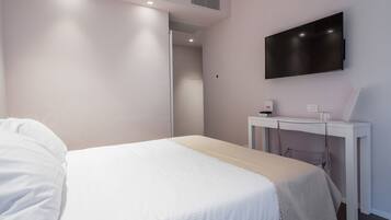 A hotel room with a bed, a desk with a flat-screen TV, and a door leading to another room.