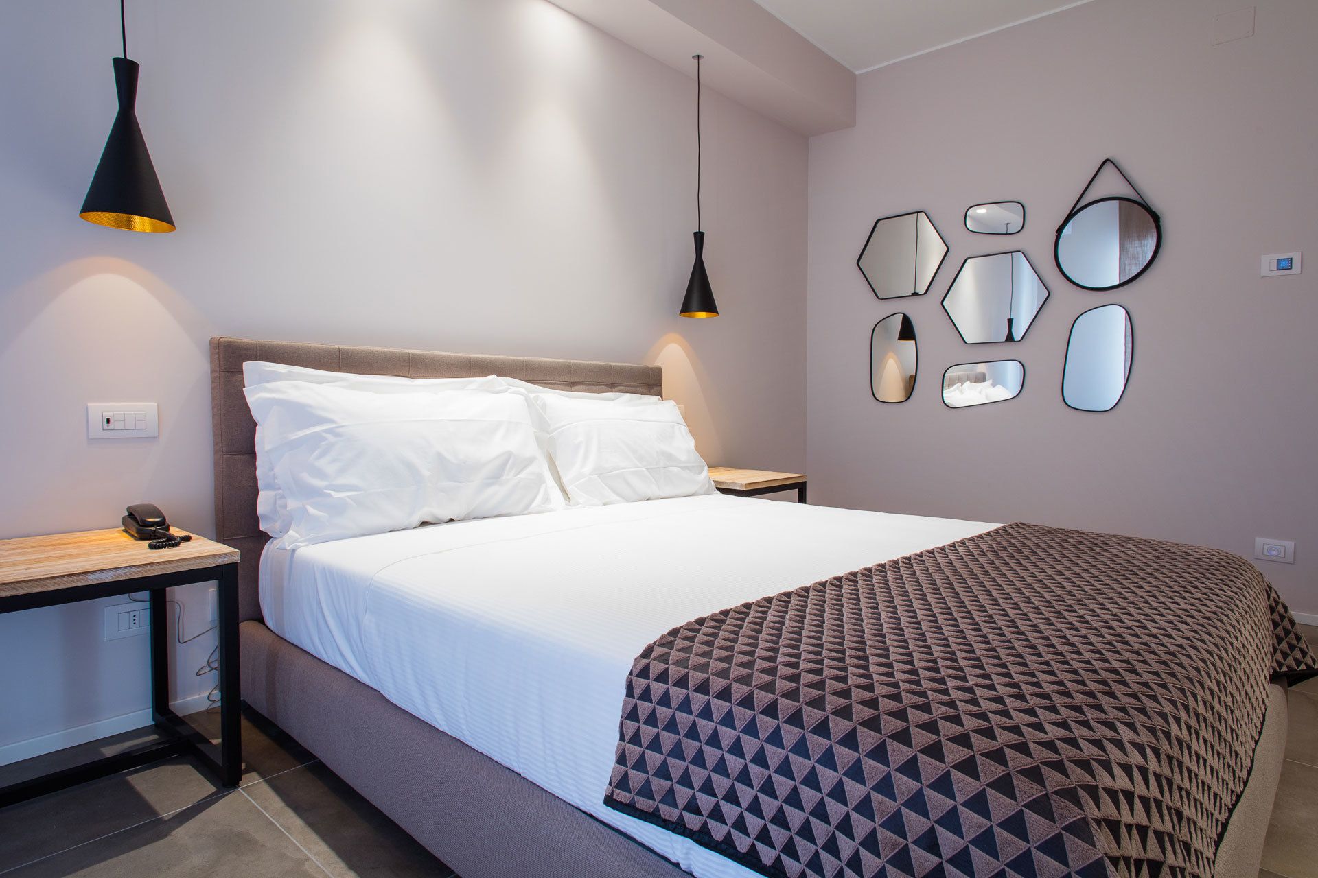 Un dormitorio moderno con una cama, dos mesitas de noche, un espejo en la pared y un enchufe.