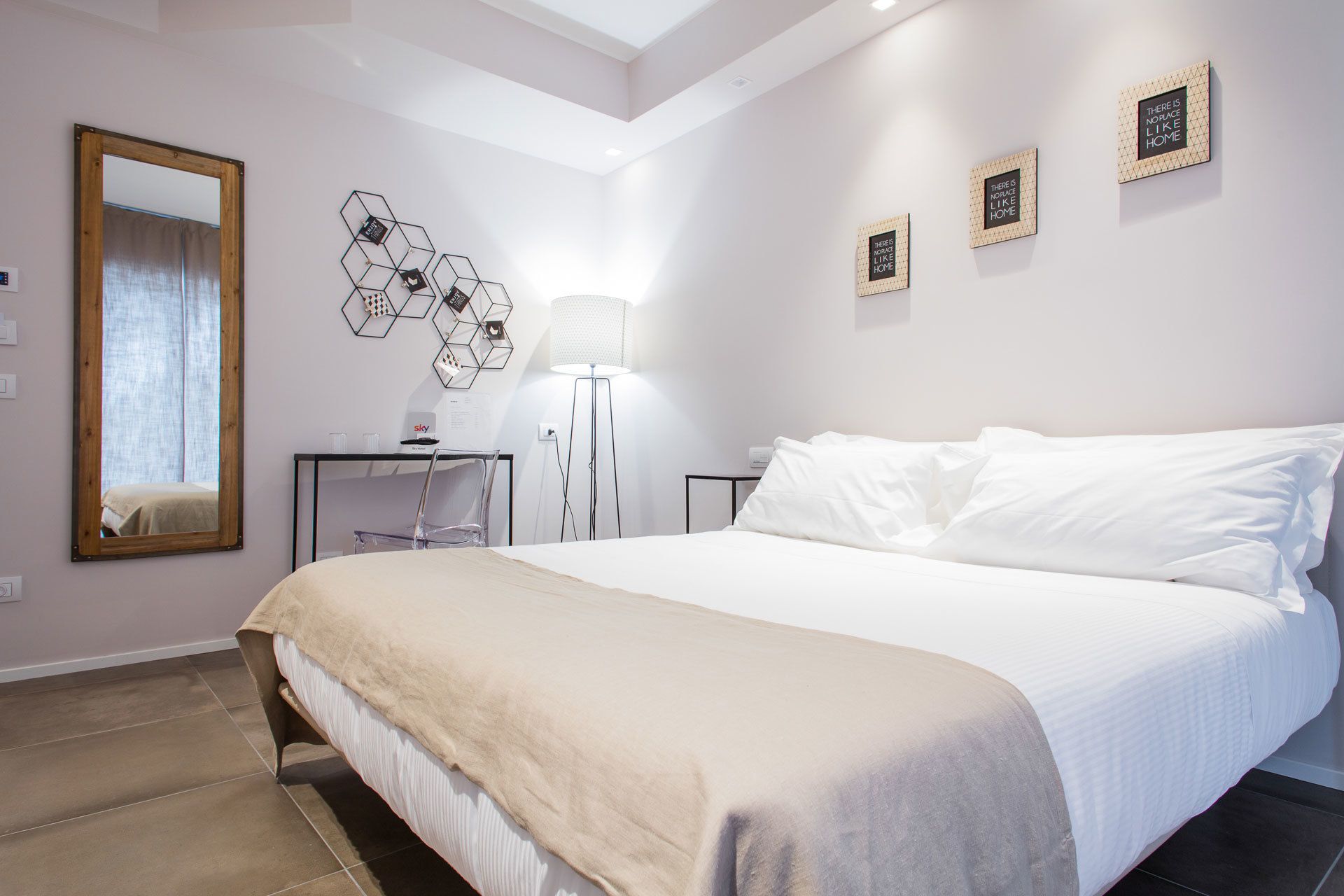 A modern bedroom with a large bed, a desk, and a chair. There are three framed motivational quotes on the wall.