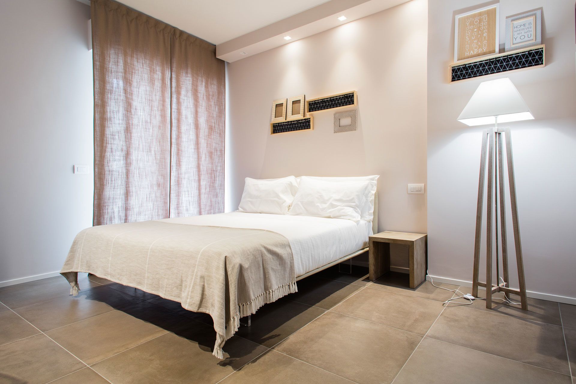 Un dormitorio con cama, mesitas de noche, una lámpara de pie y decoración en la pared.