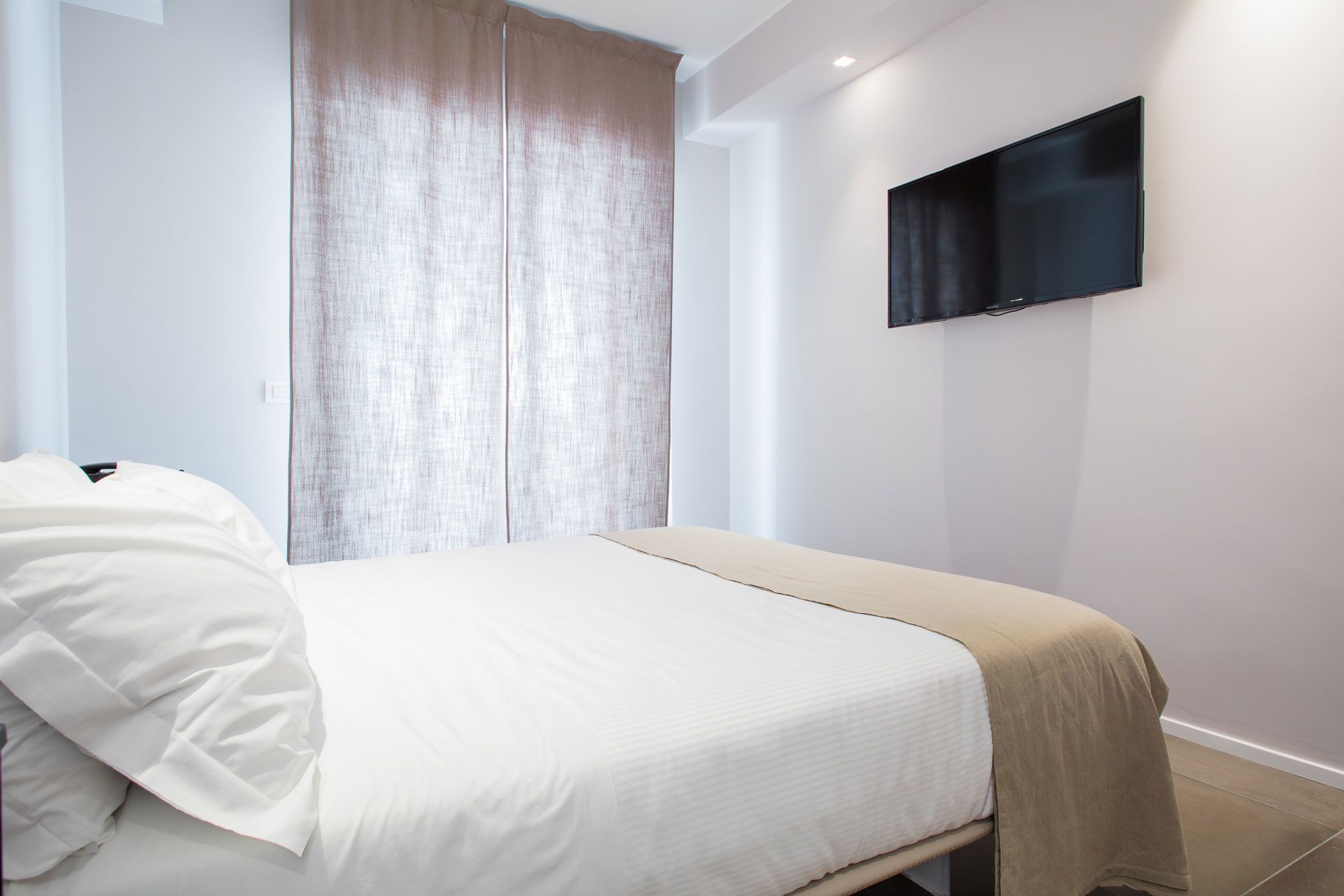 A modern bedroom with a bed, a TV mounted on the wall, and a sliding door.